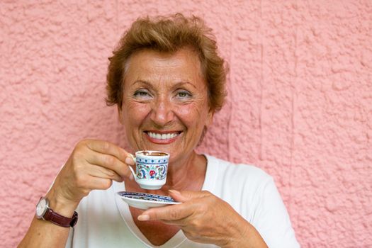 Older Lady drinking her Turkish coffee infront of pink  textured wall