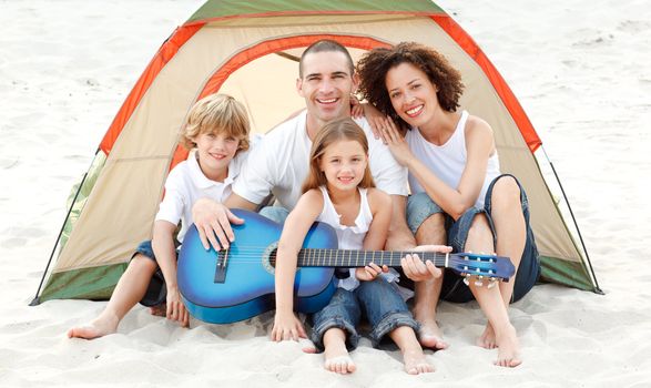 Happy family camping on beach playing a guitar