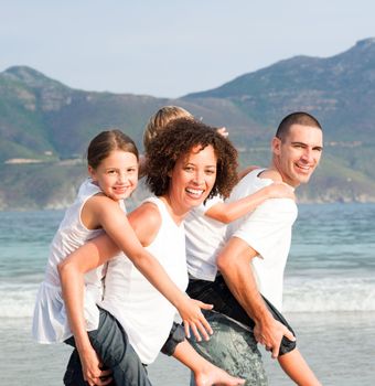 Parents giving two young children piggyback rides on the beach