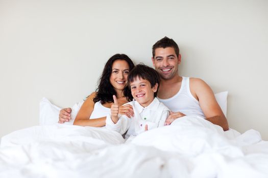 Happy child with thumbs up and his parents in bed