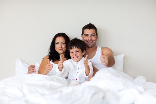 Smiling little boy with thumbs up and his parents in bed