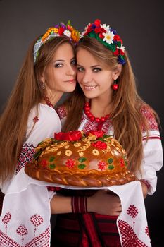 Young women in ukrainian clothes, with garland and round loaf on black background