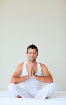 Young man sitting on bed meditating with copy-space