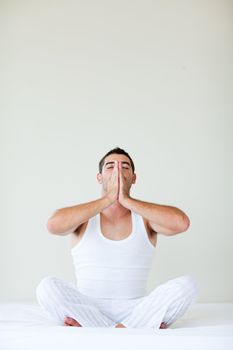 Attractive young man doing yoga sitting in bed