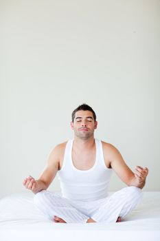 Young man sitting on bed meditating