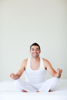 Smiling young man sitting on bed meditating
