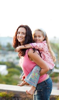 Mother giving daughter piggyback ride outdoors smiling
