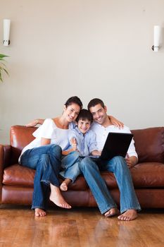 Parents and kid using a laptop with thumbs up on a couch and copy-space