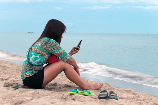 Asian woman use mobile phone on the beach.
