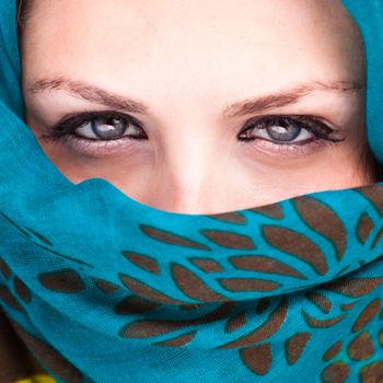 Beautiful Arab woman wearing blue scarf, stylish female close up face portrait, serious expression, stunning sensual beauty.