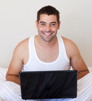 Handsome man using his laptop on the bed at home