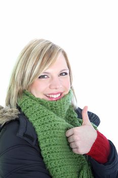Smiling attractive young woman in winter attire wrapped up in a thick coat and scarf giving a thumbs up gesture of approval