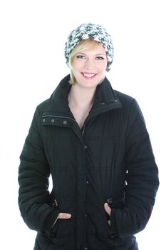 Pretty smiling woman in winter coat and knitted cap standing in a relaxed position with her hands in her pockets isolated on white