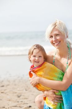 A cheerful girl in a towel and her smiling  mother at the beach