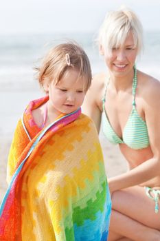 An interested girl in a towel and her mother watching to the ground at the beach
