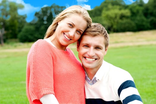 Portrait of young couple outdoors sitting on green grass. Blue sky background