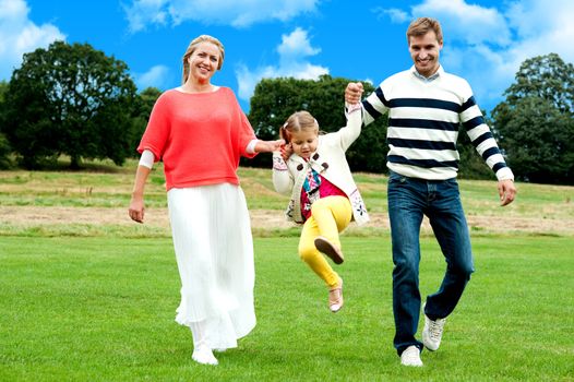 Young girl leaping high above the ground. Parents holding each hand