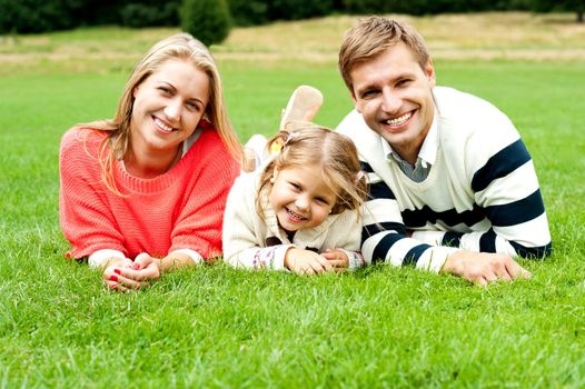 Young family of three spending a happy day outdoors. Relaxing on lush green grass