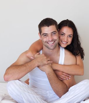 Smiling beautiful girl hugging her attractive boyfriend sitting in a bed