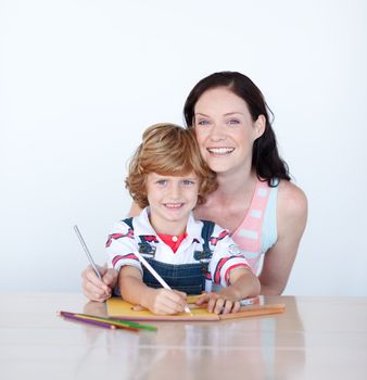 Mother and son writing at home and smiling to the camera 