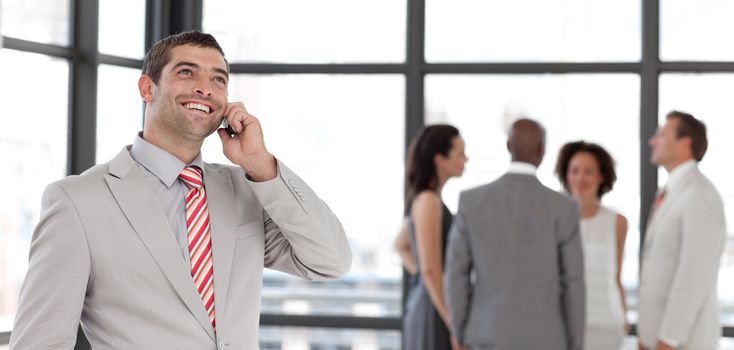 Dynamic businessman holding a phone at workplace with his colleagues in the background