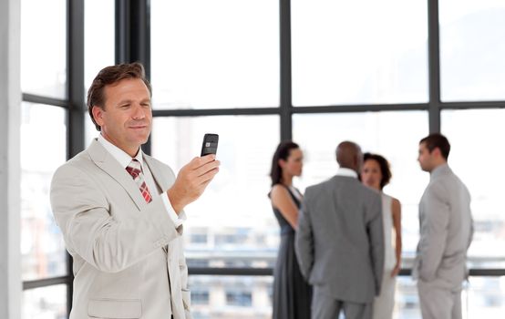 Caucasian businessman holding a phone at workplace with his colleagues in the background