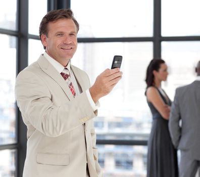 Happy businessman holding a phone at workplace with his colleagues in the background