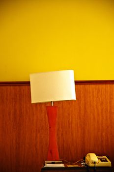 A lamp and telephone on a desk with a yellow and wood wall.