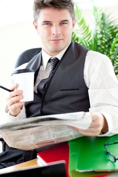 Serious businessman drinking a coffee while reading a newspaper sitting at his desk