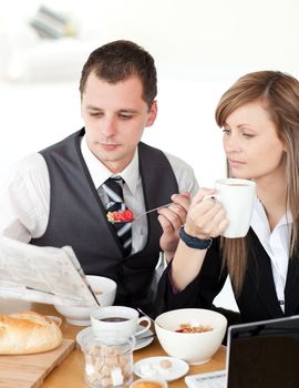 Young couple of business people reading a newspaper while having breakfast at home 