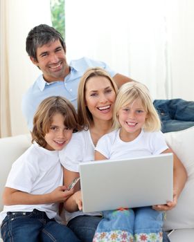 Cute children with their parents using a laptop sitting on sofa