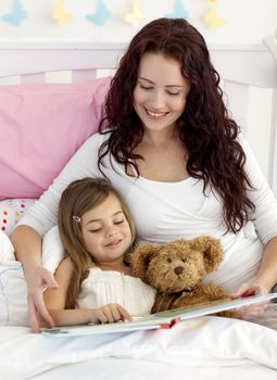 Happy mother and daughter reading a book together in bed