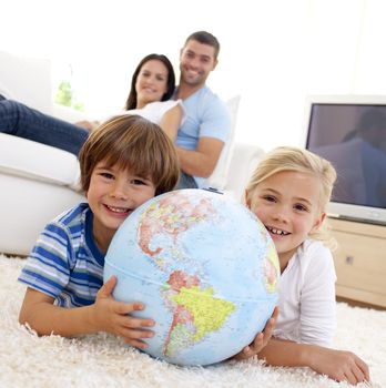 Children playing with a terrestrial globe at home with their parents on sofa