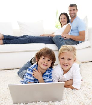 Children playing with a laptop on floor and parents lying on sofa