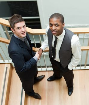 High view of Two businessmen shaking hands on stairs and smiling at the camera