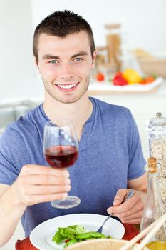 Cute man eating a healthy salad with some wine at home