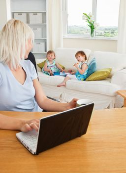 Blond mother working at laptop in living room