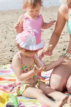 Sweet little girl using suncream at the beach with her family