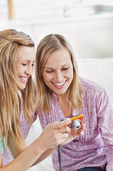 Two gorgeous women using a digital camera at home on a sofa