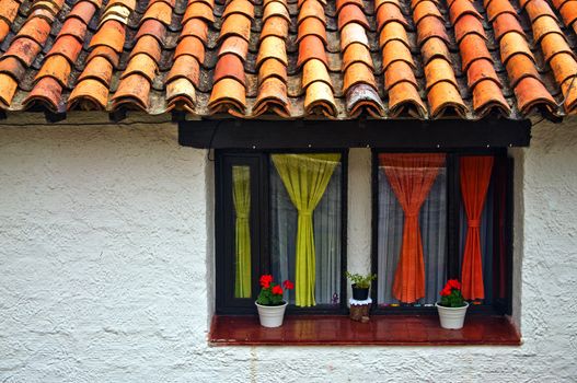 A window with a colonial style wall with colorful curtains.