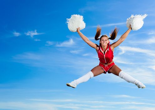 Young cheerleader in red costume jumping against blue sky