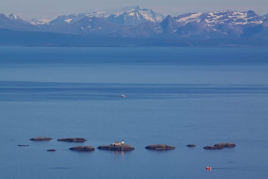 Lighthouse on tiny rocky islets near Lofoten islands with mountainous norwegian coast in the background