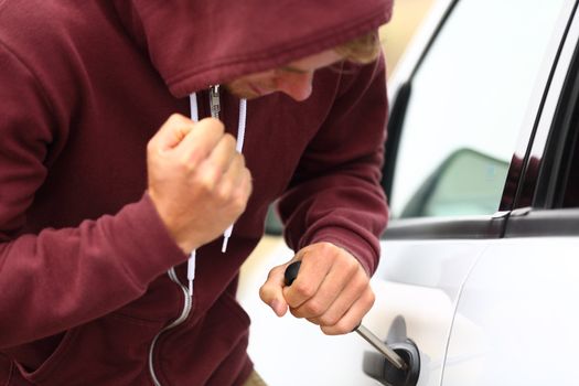 Young thug stealing a car forcing a screw driver into the door lock and hammering at it with his fist