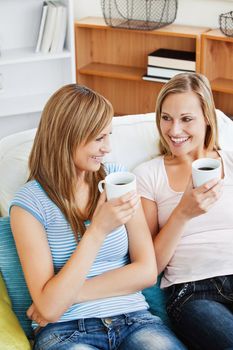 Two bright women drinking coffee together on a sofa at home