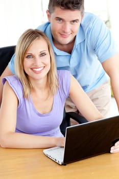 Joyful couple using a laptop sitting in the kitchen at home