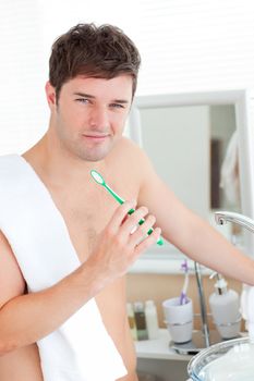 Positive young man with a towel brushing his teeth in the bathroom at home