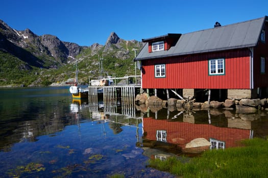 Typical red modern fishing hut on Lofoten islands in Norway reflecting in fjord