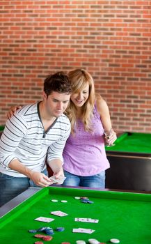 Cheerful couple playing cards on a billiard in a snooker club