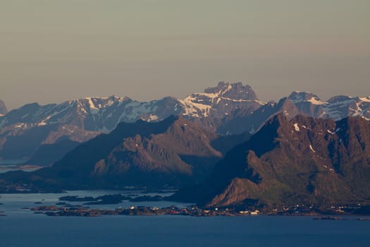Scenic mountain peaks on Lofoten islands in Norway lit by midnight sun with small fishing village by the coast