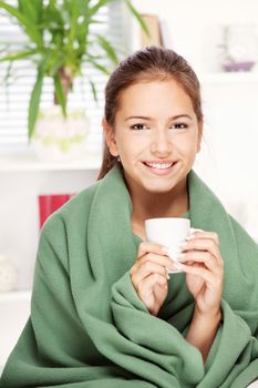 pretty young woman drinking tea  at home covered with blanket